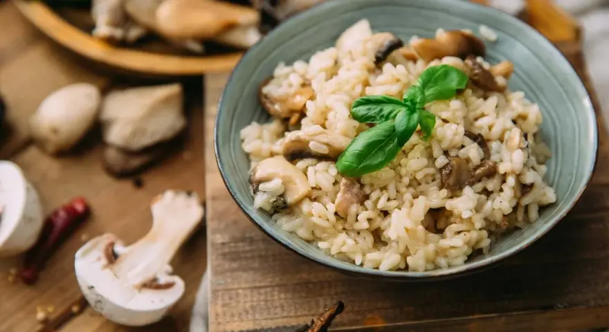 Miseczka kremowego risotto z grzybami i bazylią, otoczona świeżymi grzybami i przyprawami.