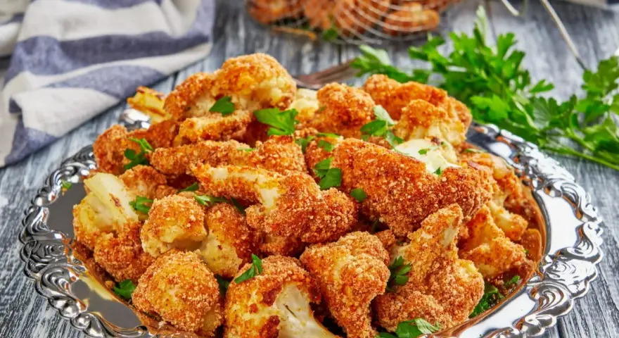 Chrupiący kalafior w panko, podany na ozdobnej tacy, posypany świeżą natką pietruszki. Idealna przekąska!
