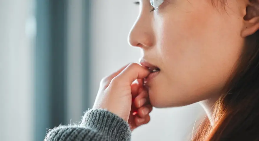 Une jeune femme songeuse, les doigts près de la bouche, réfléchit à comment arrêter de se ronger les ongles.