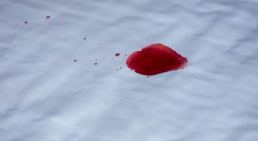 Une tache de sang rouge vif sur un tissu blanc. L'eau oxygénée pourrait aider à nettoyer cette tache.