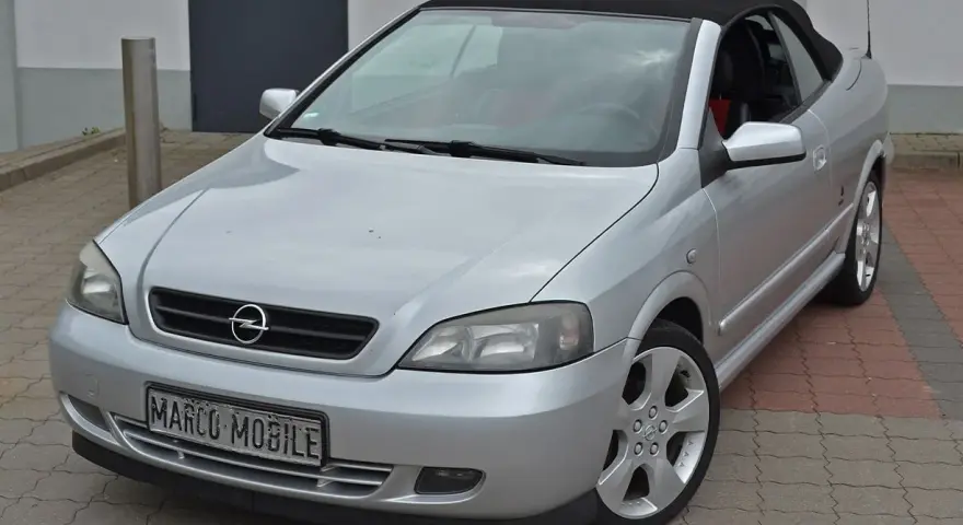 Silberner Opel Astra Bertone Cabrio mit offenem Verdeck, bereit für eine Spritztour.