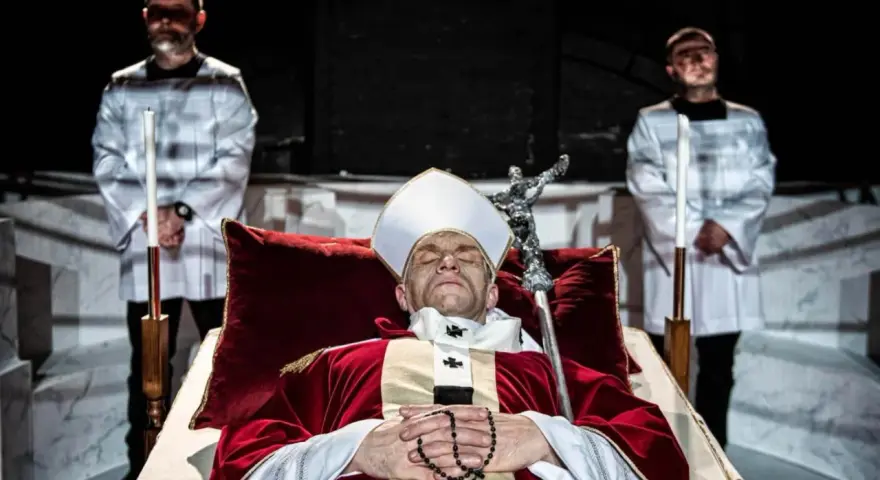 Papież w stroju, z różańcem, leży w trumnie. Obok stoją dwaj mężczyźni w białych szatach. Czy to bluźnierstwo, co to?