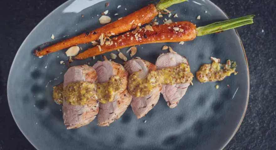 Perfekt gebratenes Schweinefilet mit Honig-Senf-Sauce und karamellisierten Karotten, bestreut mit Mandelsplittern.
