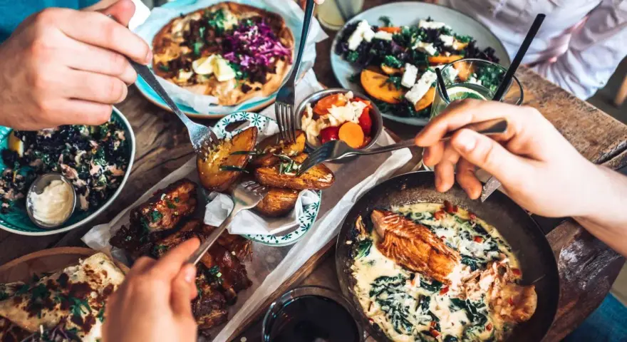 Leckeres Essen in einem Restaurant in Berlin Mitte: Pizza, Lachs, Rippchen und Salate werden von mehreren Händen geteilt.