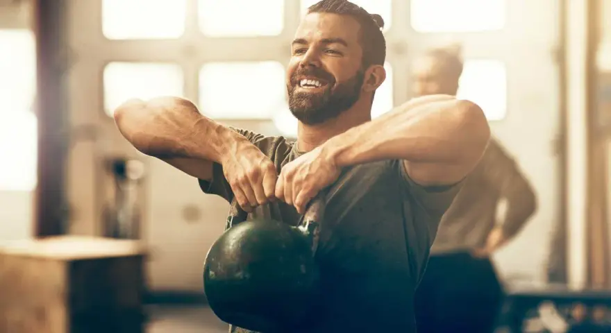 Un homme souriant effectue un exercice kettlebell, concentré sur son entraînement.