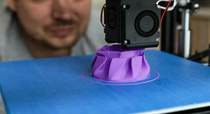 A man watches his 3D printer create a purple object, showcasing its precise 3D printer specifications in action.