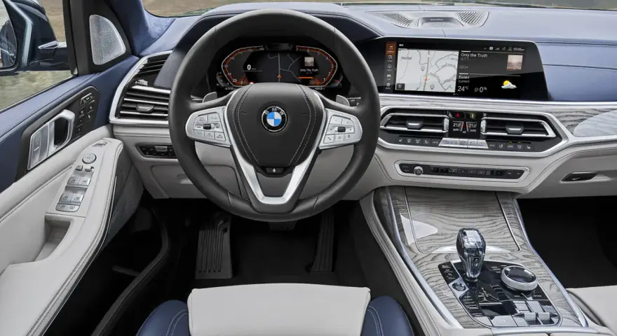 Wnętrze BMW X7: kierownica, ekran multimedialny z nawigacją i muzyką, panel klimatyzacji, dźwignia zmiany biegów.
