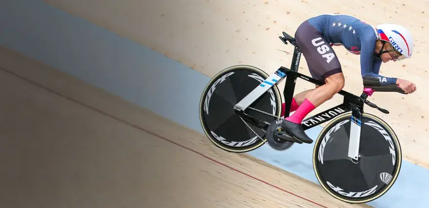 A determined track cyclist in a USA kit races on a wooden velodrome, pushing hard for victory.