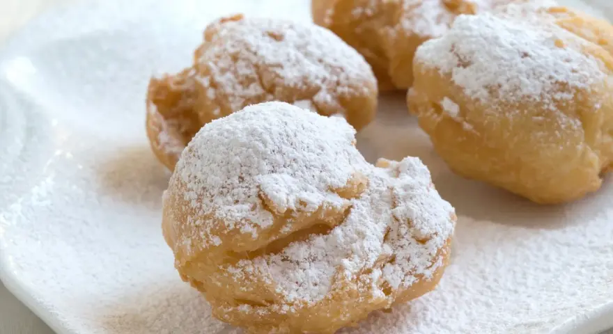 Vier goldbraune rheinische Krapfen, bestäubt mit Puderzucker, liegen auf einem weißen Teller.