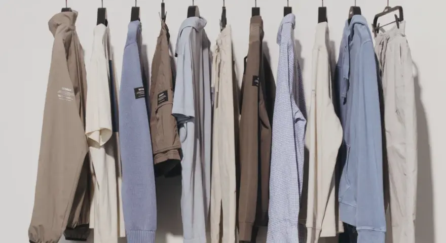 Una fila di abiti casual da uomo, con un'estetica che richiama il significato di moda evergreen: giacche, maglioni e pantaloni in tonalità neutre.