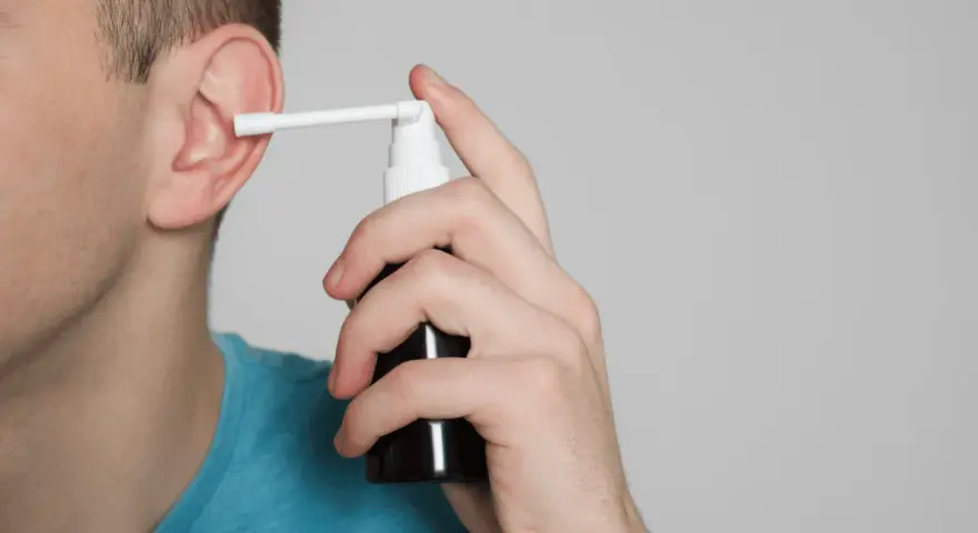 Mężczyzna aplikuje spray do ucha, łagodząc płyn w komórkach wyrostka sutkowatego.