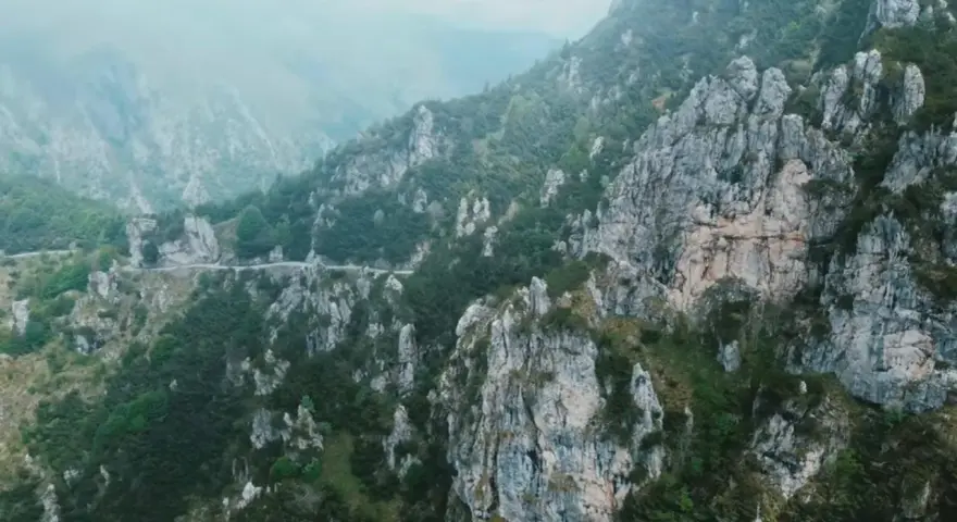 Strada tortuosa che sale verso il passo Barmone, tra rocce imponenti e vegetazione lussureggiante.