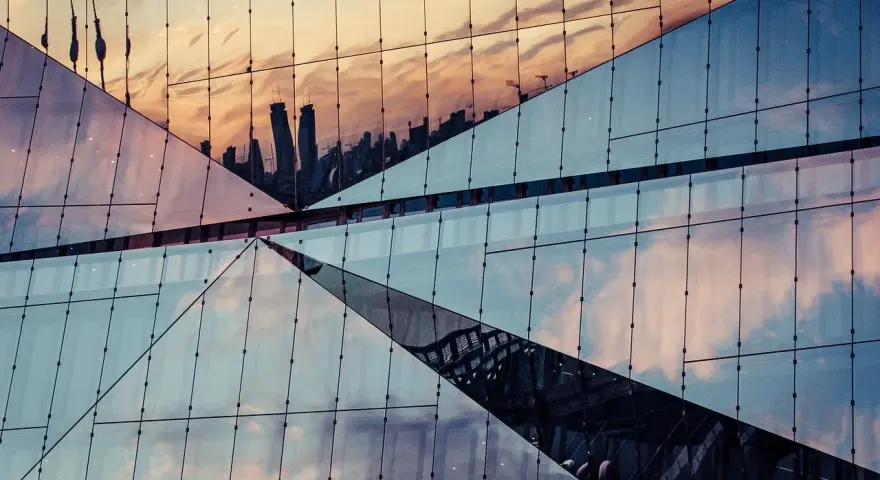 Geometryczna fasada budynku odbija niebo i sylwetki wieżowców. Efekt lustrzane odbicie photoshop.