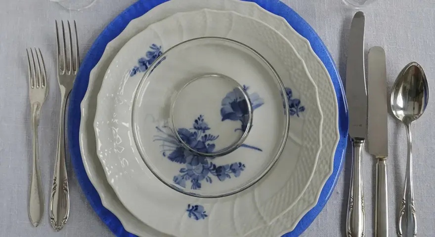 Vacker dukning med blå och vit porslin, bestick och glas. En elegant dessert tallrik väntar på att fyllas.