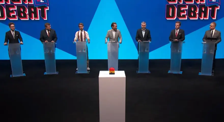 Siedmiu mężczyzn w garniturach stoi za mównicami. W tle logo "Liga Debat #2".