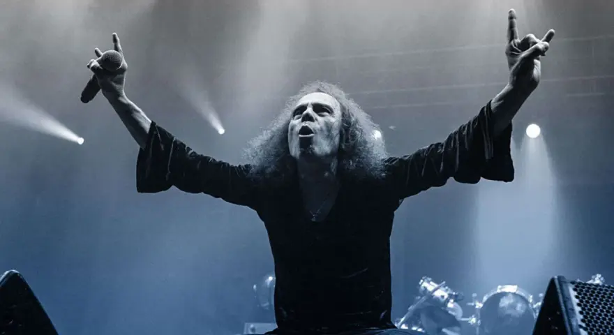 Ronnie Dio mit erhobenen Armen und Mikrofon, die Hand zum "Rock on"-Gruß geformt.