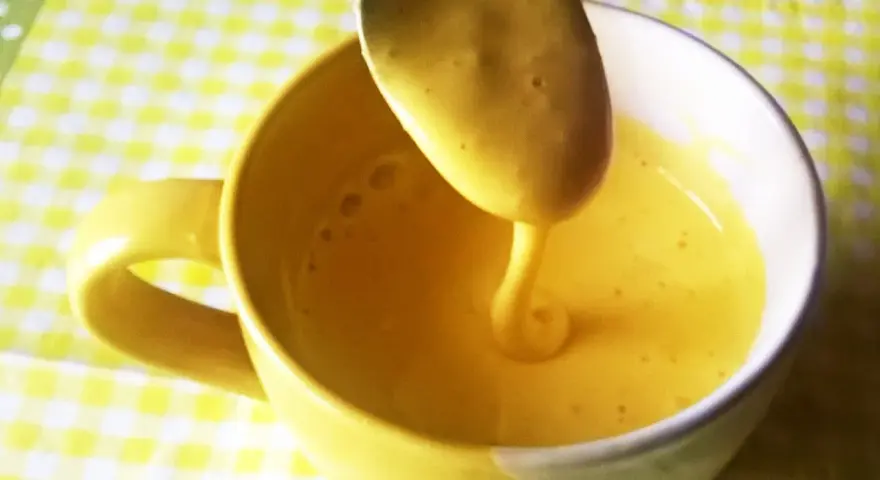 Kogel mogel przepis w filiżance, łyżka z gęstym, żółtym kremem spływa do naczynia.