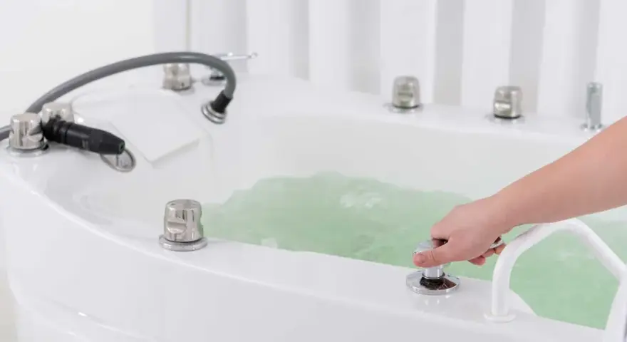 Dłoń reguluje strumień wody w wannie, przygotowując relaksujący masaż wirowy.