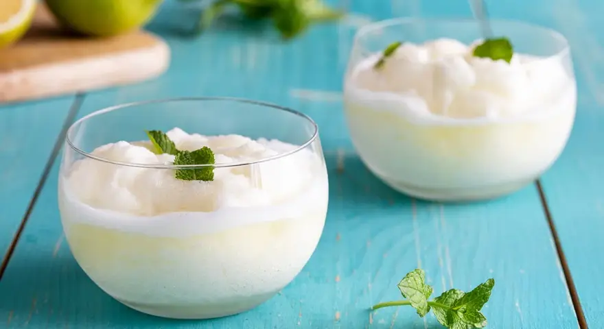 Due bicchieri di sorbetto al limone senza albume, guarniti con menta fresca, su un tavolo di legno blu.