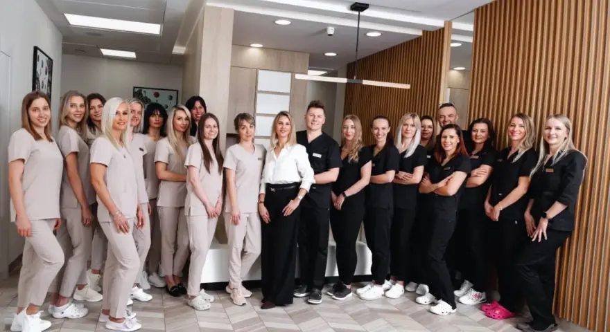 Grupa uśmiechniętych dentystów i personelu medycznego w jasnych i ciemnych uniformach stoi w nowoczesnym gabinecie.