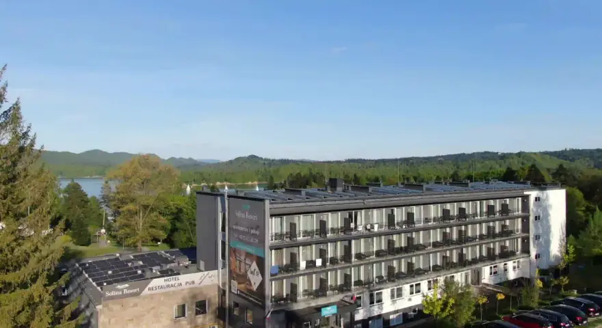 Widok na hotel Solina Resort & Spa z apartamentami i pokojami, otoczony zielenią, z jeziorem Solina w tle.