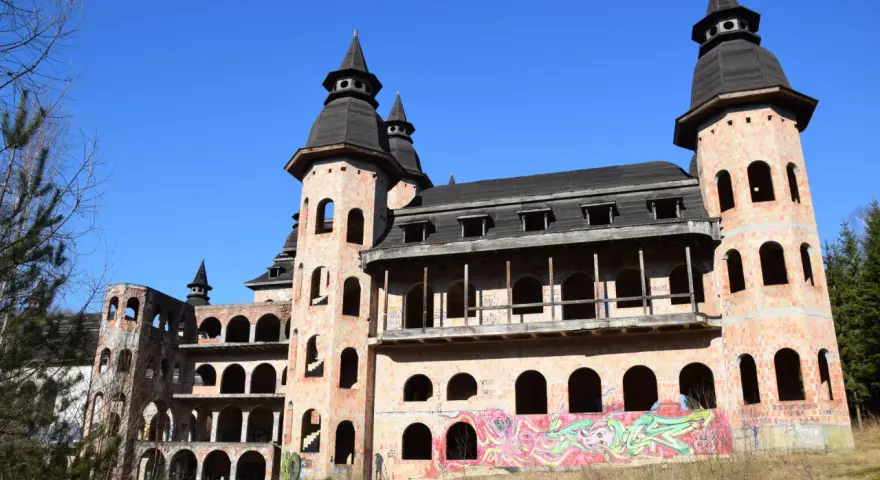 Niedokończony zamek z cegły z wieżami i graffiti na tle błękitnego nieba.