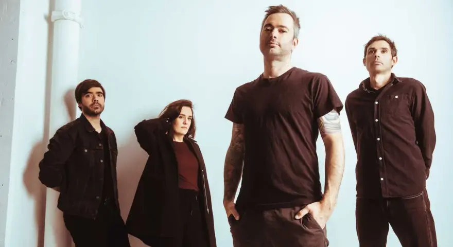 Quatre musiciens, un groupe rock canadien francophone, posent devant un mur blanc.