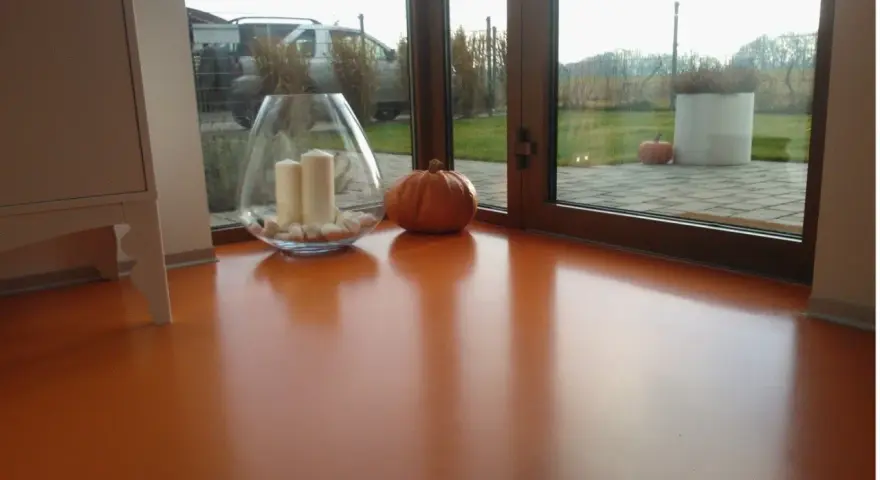 Pomarańczowa podłoga z żywicy, z widocznym blaskiem i odbiciami. Wazon ze świecami i dynia dodają jesiennego klimatu.