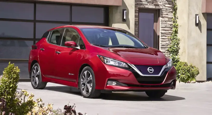 Czerwony Nissan Leaf przed nowoczesnym domem. Sprawdź atrakcyjną nissan leaf cena i wybierz swój wymarzony samochód elektryczny.