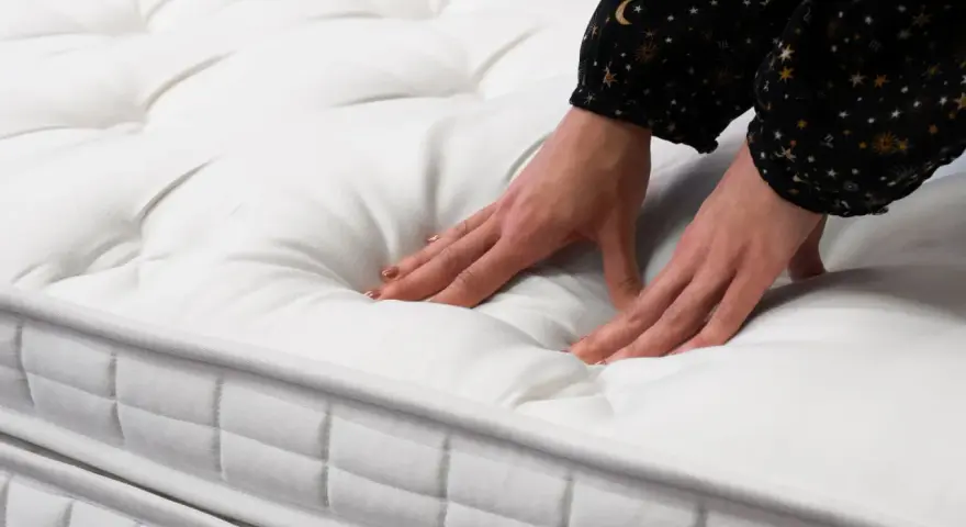 Mains testant la douceur d'un matelas blanc matelassé. Quel matelas pour mal de dos dur ou mou ? Le confort est essentiel.