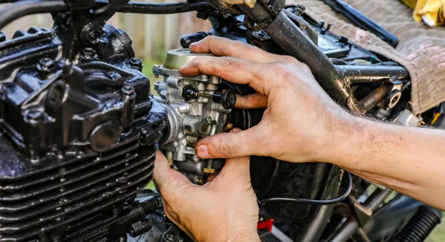 Ręce mechanika regulują gaźnik motocykla, pokazując, jak działa ssanie.