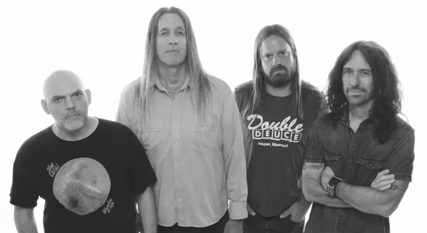 Czterech muzyków Steel Panther w Warszawie: łysy w czarnej koszulce, długowłosy w jasnej koszuli, z brodą w koszulce "Double Deuce" i w dżinsowej koszuli.
