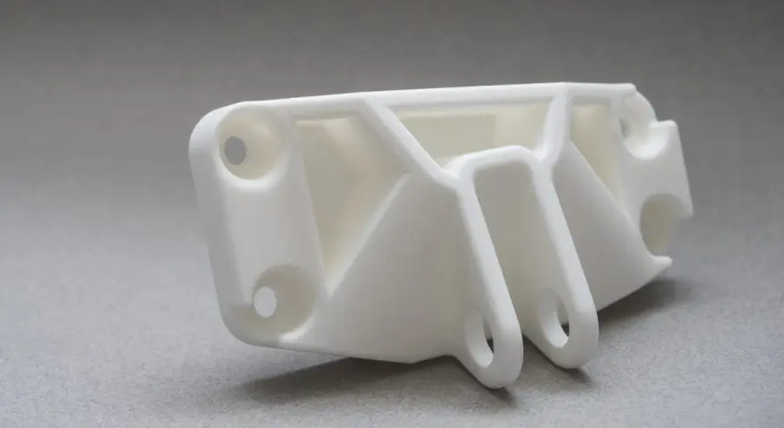 A white, complex SLS part with multiple holes and support structures, ready for assembly.