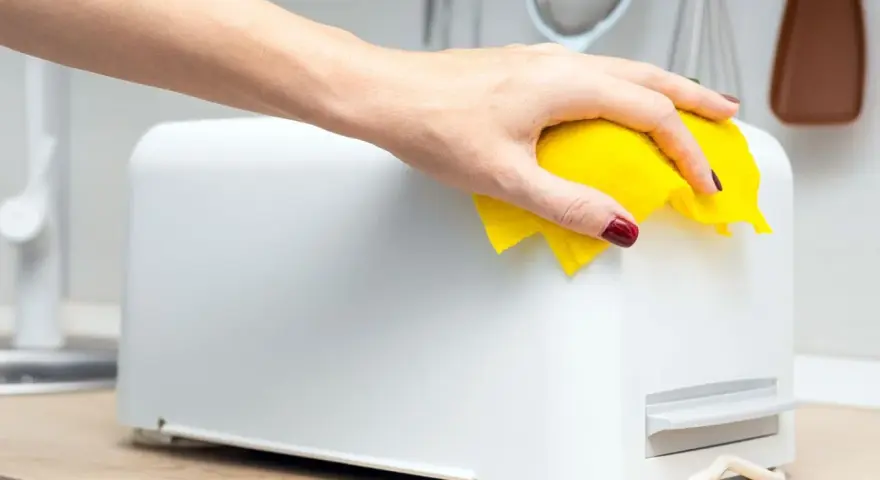 Eine Hand wischt mit einem gelben Tuch über einen weißen Toaster. So einfach ist das Toaster reinigen für ein blitzsauberes Ergebnis.