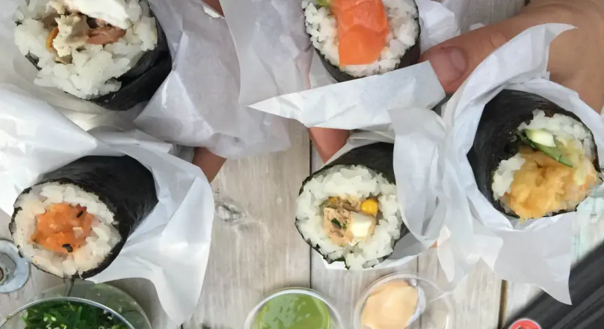 Ręcznie robione handroll sushi z łososiem, awokado, tuńczykiem i krewetkami. Pyszne przekąski na drewnianym stole.