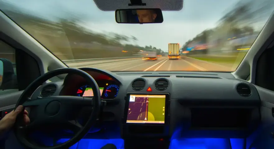 Widok z kabiny samochodu jadącego autostradą. Na desce rozdzielczej tablet z nawigacją, a obok niego system rozpoznawania znaków drogowych.