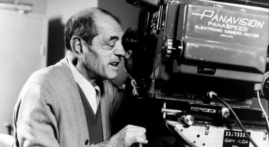 Un regista spagnolo, con un maglione grigio, guarda attraverso l'obiettivo di una cinepresa Panavision.