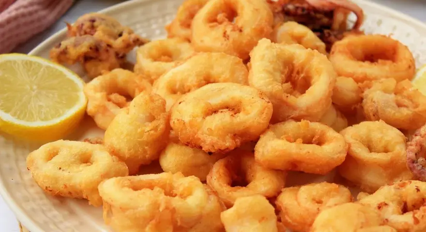Plato de calamares a la romana dorados y crujientes, servidos con rodajas de limón fresco.