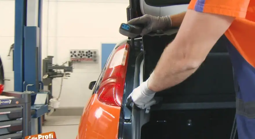Ein Mechaniker wechselt das Bremslicht eines Ford Focus. Er hält ein Werkzeug in der Hand und arbeitet am Heck des Autos.