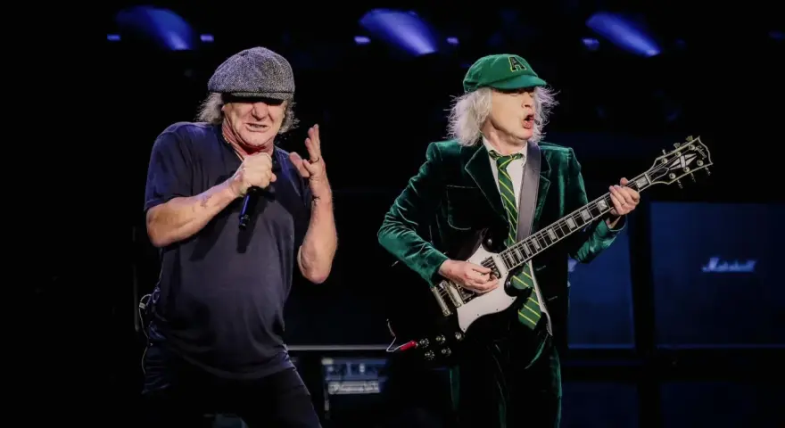 Brian Johnson i Angus Young, legendarny skład AC/DC, na scenie. Brian śpiewa do mikrofonu, Angus gra na gitarze.
