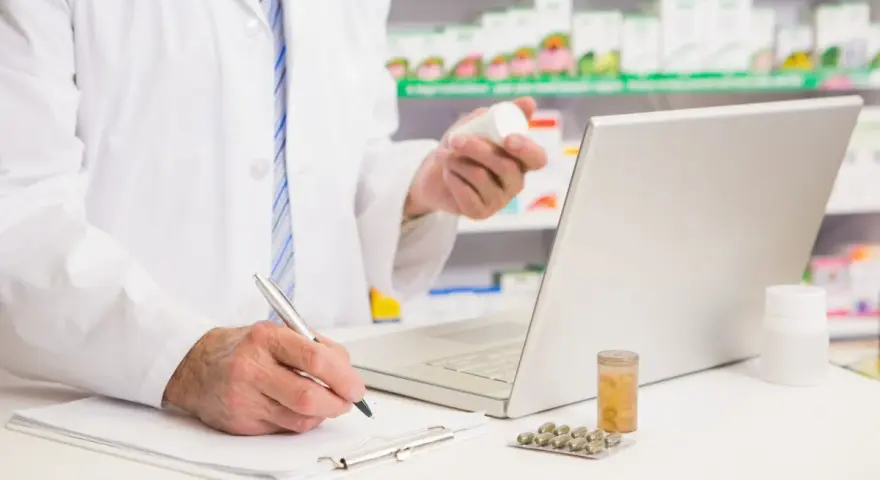 Farmaceuta sprawdza w komputerze pradaxa zamiennik, trzymając w dłoni buteleczkę leku.