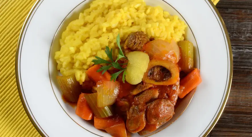 Risotto giallo e ossobuco con verdure, un classico dei piatti tipici milanesi, guarnito con prezzemolo e scorza di limone.