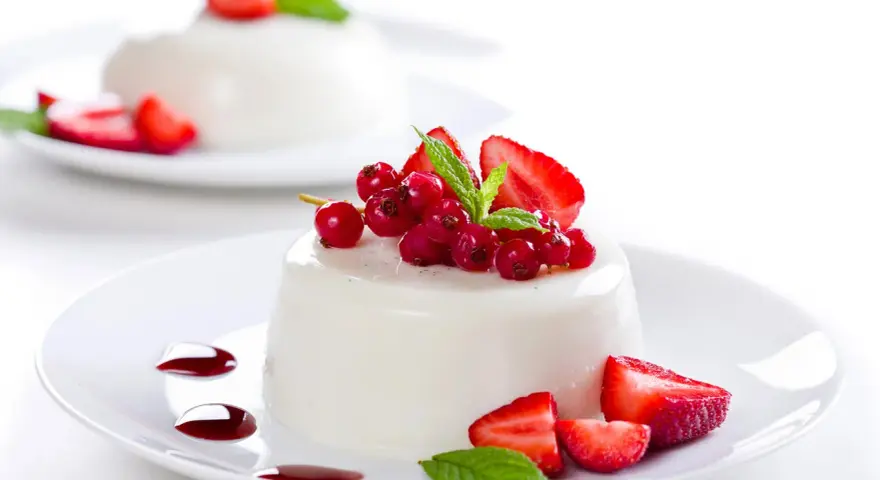 Deliciosa panna cotta cremosa adornada con fresas, grosellas rojas y menta fresca.