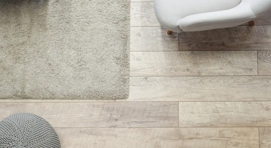 Elige el color del suelo de una casa con este suelo de madera clara, alfombra beige y puf gris.