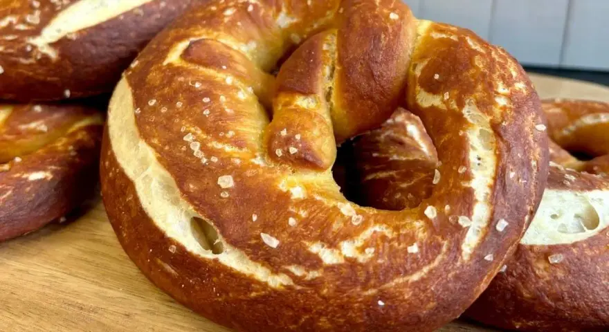 Frisch gebackene, goldbraune sauerteig brezeln mit grobem Salz bestreut, liegen auf einem Holzbrett.