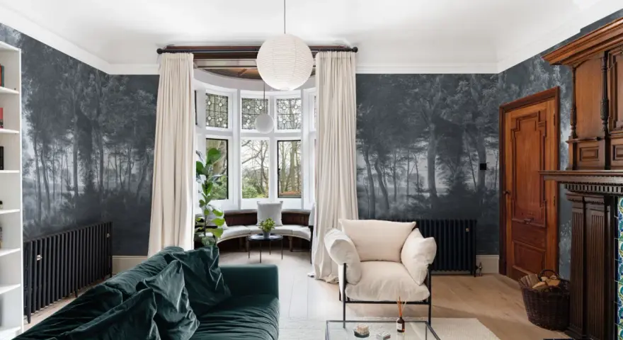 Sala con papel pintado de bosque, sofá verde, sillón beige y chimenea de madera. Ideas de como poner papel pintado para transformar tu hogar.