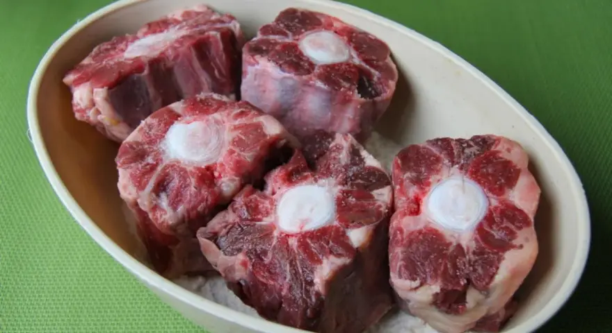 Trozo de rabo de ternera crudo en un cuenco, con el hueso central visible.