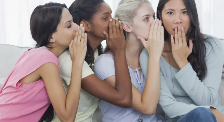 Four friends share secrets, whispering what is gossip. One girl looks surprised as the whispers continue.