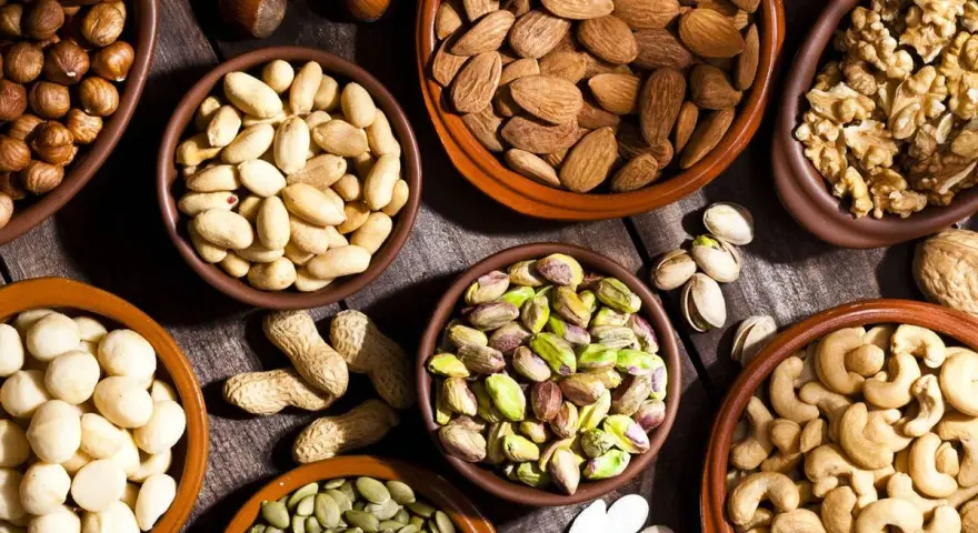 Varios cuencos de barro llenos de frutos secos variados: almendras, nueces, pistachos, anacardos, cacahuetes, avellanas y semillas de calabaza.