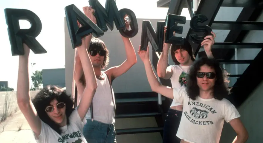 Vier Männer halten die Buchstaben des **titels von Ramones** hoch. Sie tragen Sonnenbrillen und Band-T-Shirts.